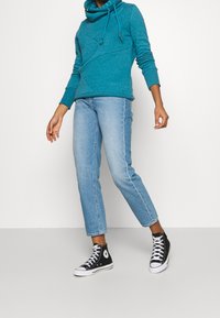 Sudadera con capucha color turquesa, con cordones ajustables, combinada con jeans rectos de color azul claro y zapatillas negras de caña alta.