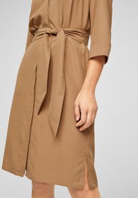 Abito marrone con cintura, realizzato in tessuto leggero. Presenta un design avvolgente, maniche a tre quarti e spacchi laterali per un tocco di stile in più.