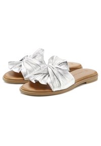 Silver metallic slide sandals feature a large bow detailing on the upper, tan footbed, and a flat rubber sole, suitable for casual wear.