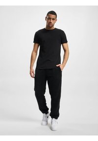 Svart bomull T-skjorte kombinert med svarte fluffy joggebukser. Joggebuksene har en teksturert overflate, og modellen har på seg hvite joggesko. Nøytral bakgrunn.