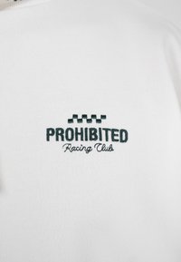 Λευκό ύφασμα με μαύρο κεντημένο κείμενο "PROHIBITED Racing Club" κάτω από ένα μαύρο καρό μοτίβο.