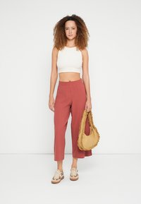 Top branco cropped leve, calças largas terracota soltas e uma bolsa castanha com borda franzida; modelo usa ténis beige.