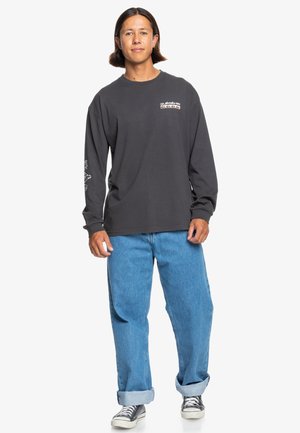 Long-sleeve dark gray t-shirt with logo print on chest and sleeve, paired with light blue loose jeans and black and white sneakers.