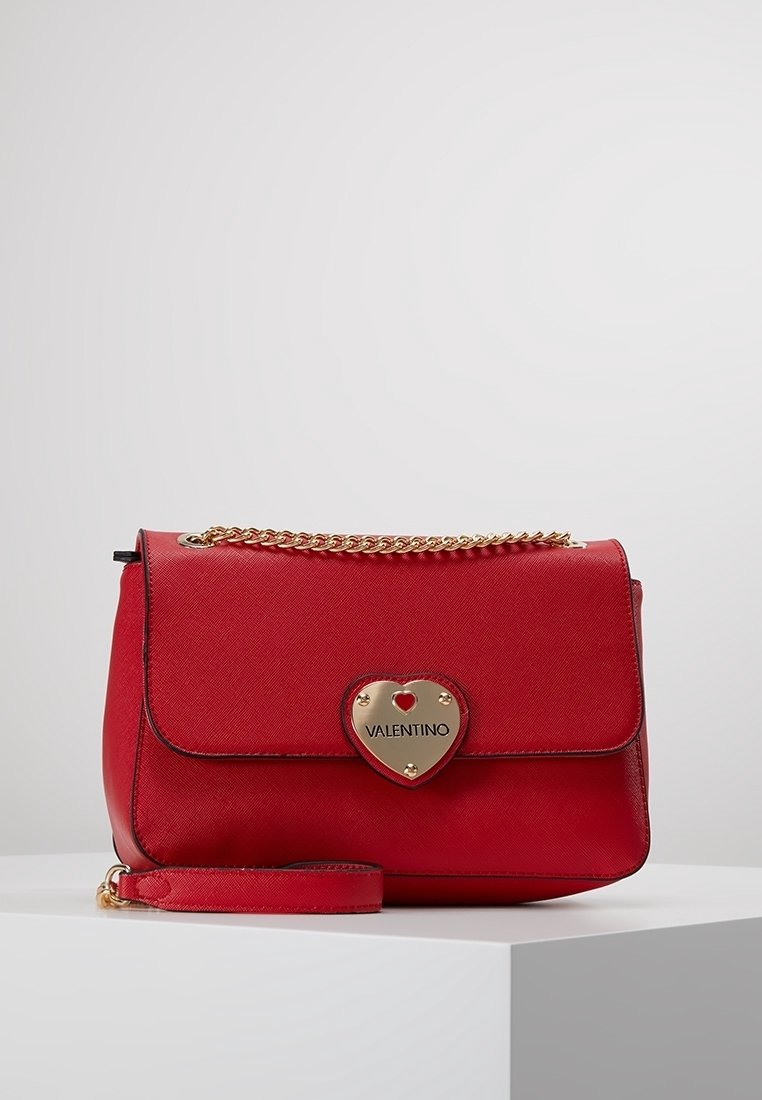 Borsa a mano in pelle rossa con finitura testurizzata, hardware a forma di cuore in oro, pattina pieghevole e tracolla a catena. Forma compatta con tracolla staccabile.