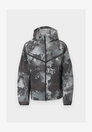 Heren jas met capuchon en volledige rits aan de voorkant, camouflagepatroon in grijstinten, zwarte chevron detail en ritszakken aan de zijkanten.