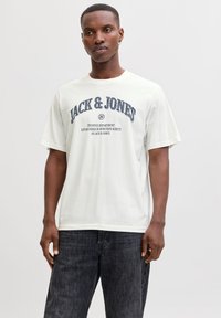 Hvid bomuld T-shirt med marinebl åt grafisk tekst "JACK & JONES" og mindre tekst nedenunder, rund halsudskæring og korte ærmer.