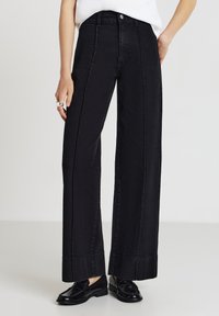 Pantaloni in denim neri a gamba larga con vita alta, con un design pulito, dettagli cuciti e una texture liscia. Abbinati a mocassini lucidi.