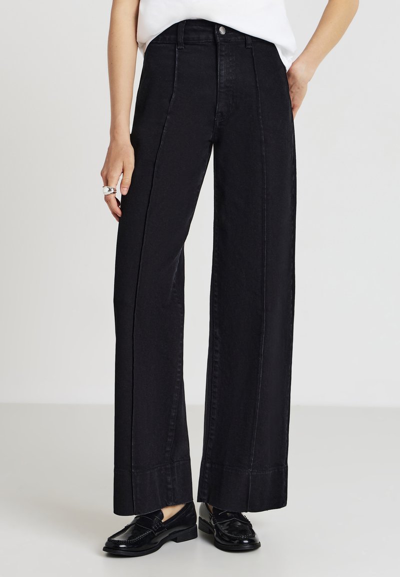 Pantaloni in denim neri a gamba larga con vita alta, con un design pulito, dettagli cuciti e una texture liscia. Abbinati a mocassini lucidi.