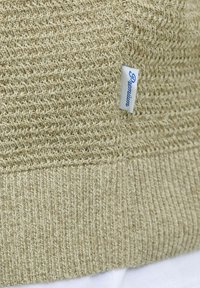 Pull en tricot beige avec un motif texturé et un ourlet côtelé, portant une étiquette bleue « Premium ». Matière douce et design décontracté.