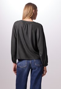 Blusa nera in seta con maniche lunghe e voluminose e scollo arricciato sul retro, abbinata a jeans in denim blu a vita alta.