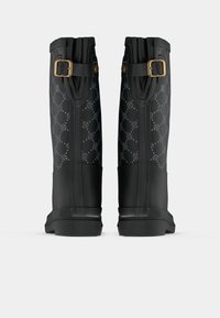 Bottes noires jusqu'au genou avec une finition brillante à motifs, dotées d'un accent en boucle en or et d'une semelle en caoutchouc noir texturé.