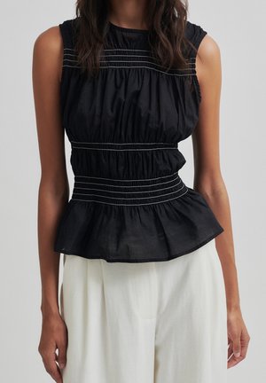 Ärmellose schwarze Bluse mit weißen horizontalen Nähten, geraffter Taille und Schößchen-Saum, getragen mit weißen Hosen an einer Person.