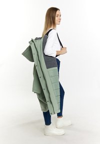 Geacă puffer de culoare verde deschis cu accente gri, având închidere cu capse și croi oversized. Asortată cu blugi skinny de culoare albastru închis și adidași albi.