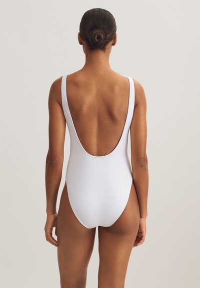 Vit baddräkt med tunna axelband, låg rygg och minimalistisk design. Slät, stretchig tyg utan mönster eller utsmyckningar.
