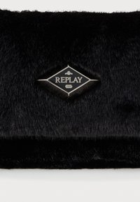 Crna clutch torbica od umjetnog krzna s logom u obliku dijamanta od srebra na kojem je napisano "REPLAY" i godina "1981" utisnuta na crnoj pozadini.