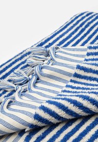 Toalla de algodón con rayas azules y blancas, con flecos en un lado. La textura es de bucles y tejido, lo que le da una apariencia suave.