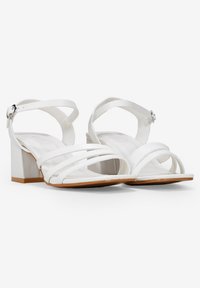 Sandalias de tacón blanco con correas delgadas, hebilla ajustable en el tobillo, tacón cuadrado y acabado suave. Suela de goma con acentos en marrón claro.