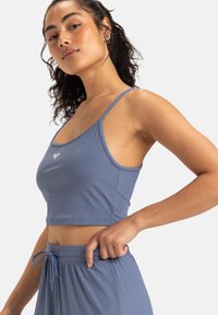 Top corto azul de canalé con tirantes finos, que presenta un pequeño logotipo en la parte delantera. Combinado con pantalones de talle alto a juego.