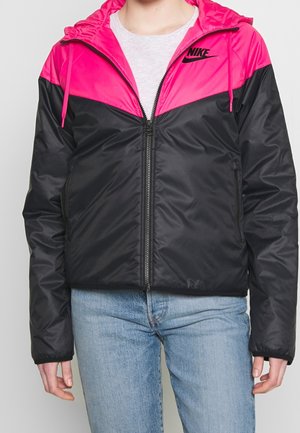Personne portant une veste zippée avec une capuche rose vif et le haut de la poitrine, partie inférieure noire, et logo Nike sur le côté gauche de la poitrine.
