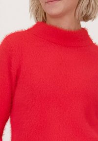 Rode trui met een zachte, pluizige textuur, voorzien van een hoge nek en lange mouwen. Het materiaal lijkt dik en warm, met een uniforme kleur.