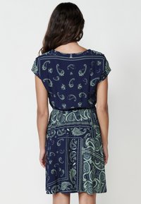 Rochie de marină cu modele paisley în verde deschis, mâneci scurte și talie elastică, având o siluetă fluentă și o textură moale a fabricii.