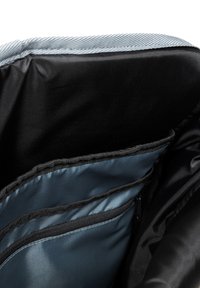 Czarny materiał wewnętrzny plecaka, z niebieskimi i szarymi przegródkami, zamkami błyskawicznymi oraz teksturowanymi krawędziami, zapewniającymi organizację i strukturę.