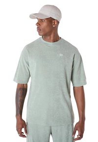T-shirt vert clair à manches courtes en tissu doux avec une finition texturée et un petit logo sur la poitrine. Associé à une casquette assortie.