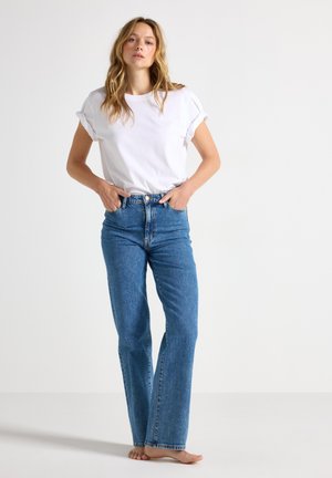 Maglietta bianca in cotone con maniche arrotolate, abbinata a jeans in denim blu a vita alta con taglio dritto e cuciture a vista.
