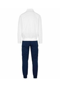 Giacca bianca con zip e polsini e orlo a costine, abbinata a pantaloni tapered blu navy con polsini elastici. Tessuto liscio, dettagli di design minimi.