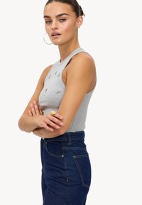 Débardeur gris à côtes avec un col montant, orné de petites embellissements en métal, associé à un jean en denim bleu foncé taille haute.