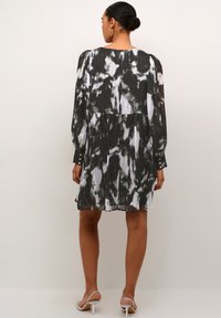 Robe plissée à imprimé abstrait noir et blanc avec des manches longues, un col rond et des poignets boutonnés, arrivant au-dessus du genou.