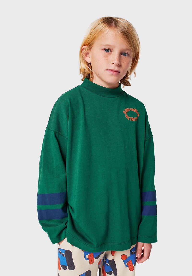 Camisa verde de algodón de manga larga con cuello alto, con texto en naranja y rayas azul marino en las mangas. Textura suave, corte relajado.