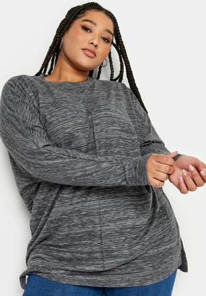 Grijze longsleeve top met een gestructureerd, licht gemarmerd patroon. Heeft een ontspannen pasvorm en een ronde zoom, gecombineerd met blauwe jeans.