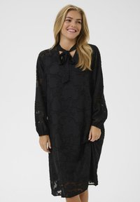 Rochie neagră din țesătură transparentă, cu mâneci lungi, un șnur la guler și un model texturat de frunze pe întreaga suprafață.