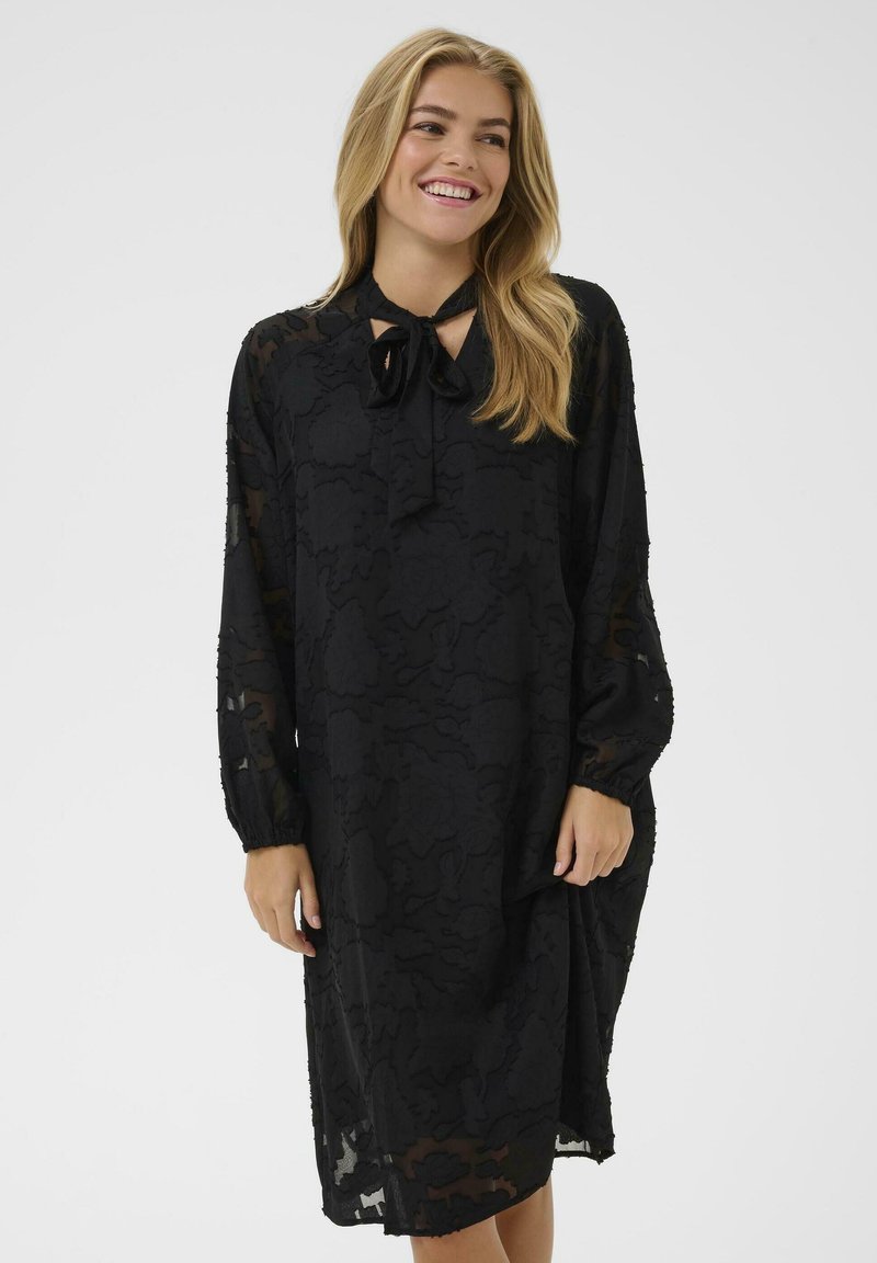 Rochie neagră din țesătură transparentă, cu mâneci lungi, un șnur la guler și un model texturat de frunze pe întreaga suprafață.