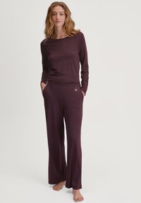 Bordeaux lange mouwen top en bijpassende wijde broek van zacht materiaal, met een zijzak en een subtiele logo op de tailleband.
