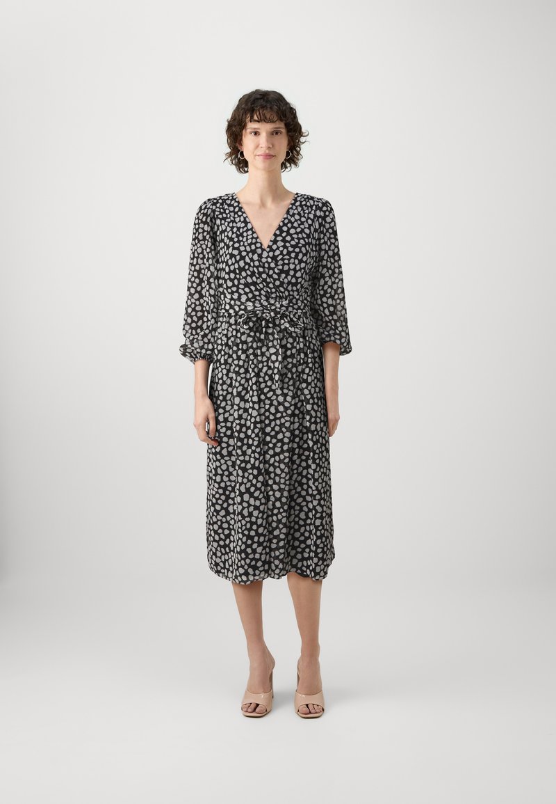 Vestido preto envolvente com padrão de bolinhas brancas, apresenta mangas longas e um cinto na cintura. Tecido suave e leve com um comprimento abaixo do joelho.