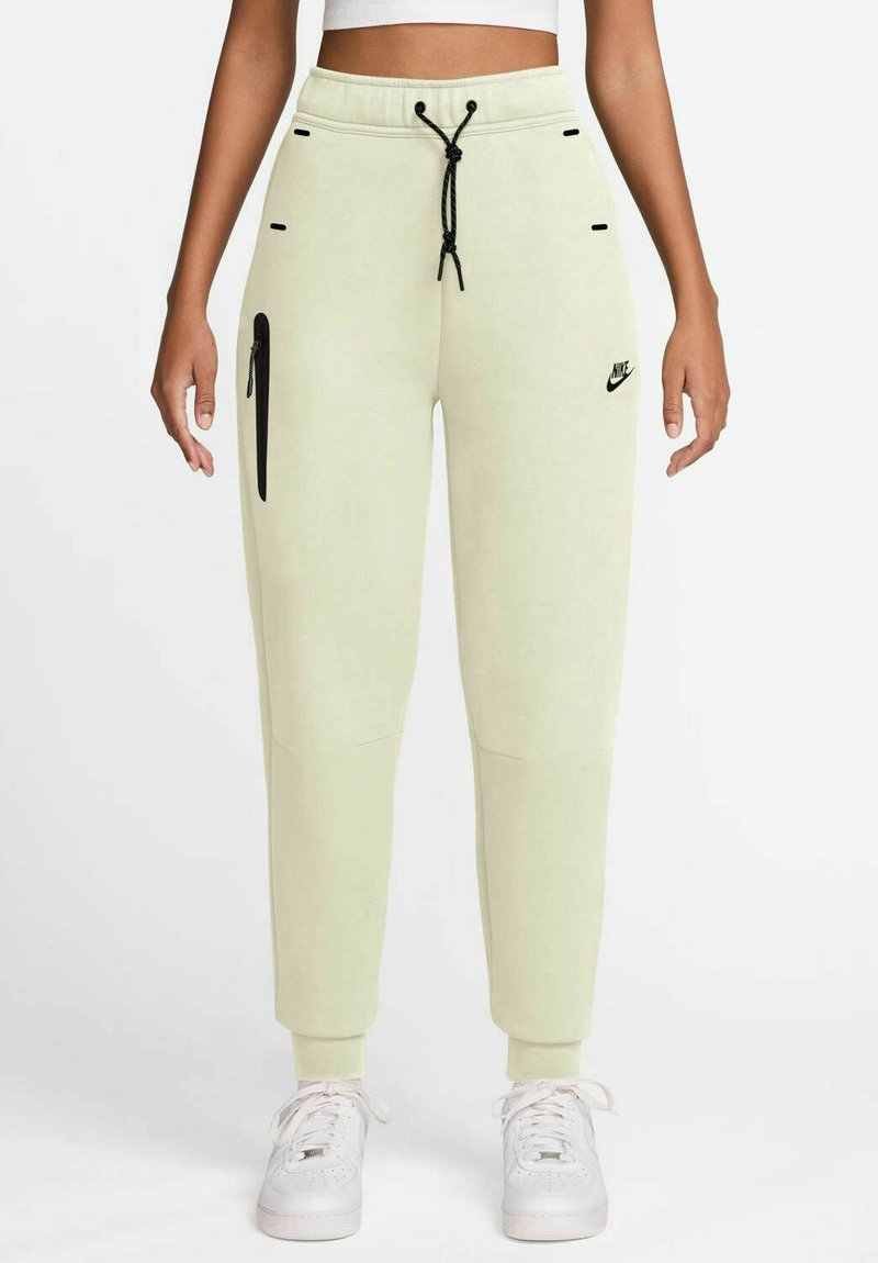Jasnozielone dresy Nike z elastyczną talią, sznurkiem, boczną kieszenią na zamek i prążkowanymi mankietami; wykonane z miękkiego materiału o gładkiej fakturze.