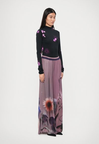 Maglietta nera a maniche lunghe con fantasie floreali rosa, abbinata a una gonna maxi fluida viola con elastico in vita. Scarpe nere.