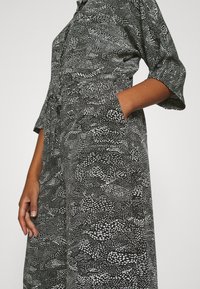 Svart och vit jumpsuit med korta ärmar, prydd med ett varierat mönster av prickar och vågor, samt sidofickor för extra funktionalitet.