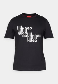 T-shirt noir à manches courtes avec texte blanc déformé épelant "Hugo" plusieurs fois en diagonale sur la poitrine.