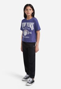 Camiseta de algodón morada con gráfico de "Nueva York", combinada con pantalones de chándal negros y zapatillas negras. Diseño simple con mangas cortas y corte relajado.