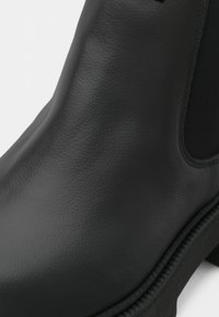 Μαύρη μπότα α ankle από υφασμάτινο δέρμα, με λείο φινίρισμα, ελαστικές πλαϊνές πάνες και ανθεκτική σόλα με έντονη ραφή.