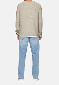 Beige gestrickter Pullover mit langen Ärmeln und einem strukturierten Muster, kombiniert mit hellblauen Denim-Jeans im lässigen Schnitt und einer entspannten, ausgewaschenen Optik.