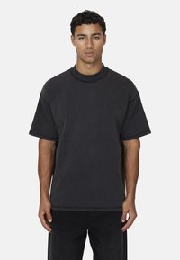T-shirt oversized in cotone nero con maniche corte e scollatura rotonda. Presenta un logo testuale in rilievo sul petto e una vestibilità strutturata.
