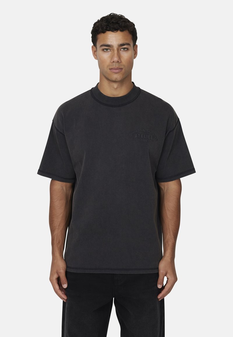 T-shirt oversized in cotone nero con maniche corte e scollatura rotonda. Presenta un logo testuale in rilievo sul petto e una vestibilità strutturata.