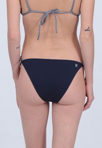 Bas de bikini bleu marine avec un tissu texturé, des liens ajustables sur les côtés et un petit logo accentué à l'arrière.