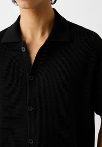 Zwarte korte mouwen shirt met een gestructureerde, gemusterde stof, een button-down kraag en zwarte knopen langs de voorkant.