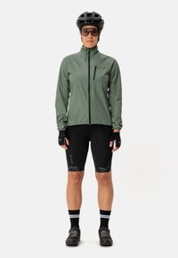 Groene lichtgewicht fietsjas met ritssluiting, zwarte gevoerde shorts met een gegolfde zoom, handschoenen, helm en zonnebril.
