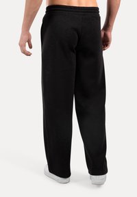 Pantalones de chándal negros con un corte holgado, cintura elástica y bolsillos laterales, hechos de una tela suave. Presenta zapatillas blancas.